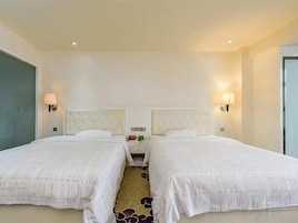 Habitación de hotel con dos camas, una mesita de noche y lámparas fijadas a la pared.