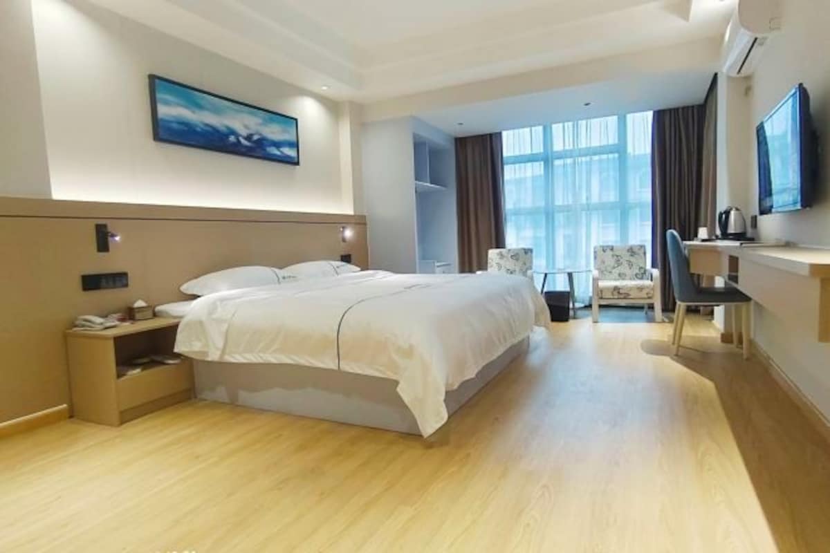 A modern hotel room with a large bed, a desk, a chair, and a TV.