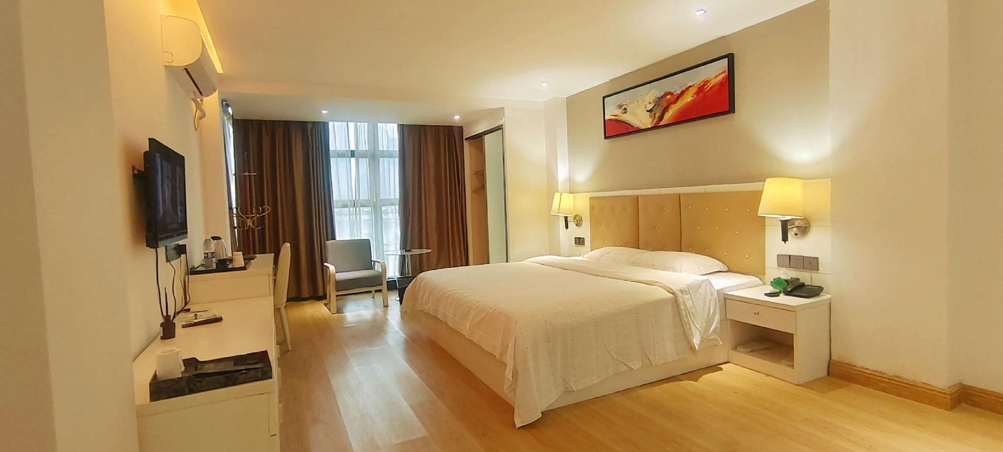 Une chambre d’hôtel avec un lit, des tables de chevet, une télévision, une chaise et un tableau au mur.