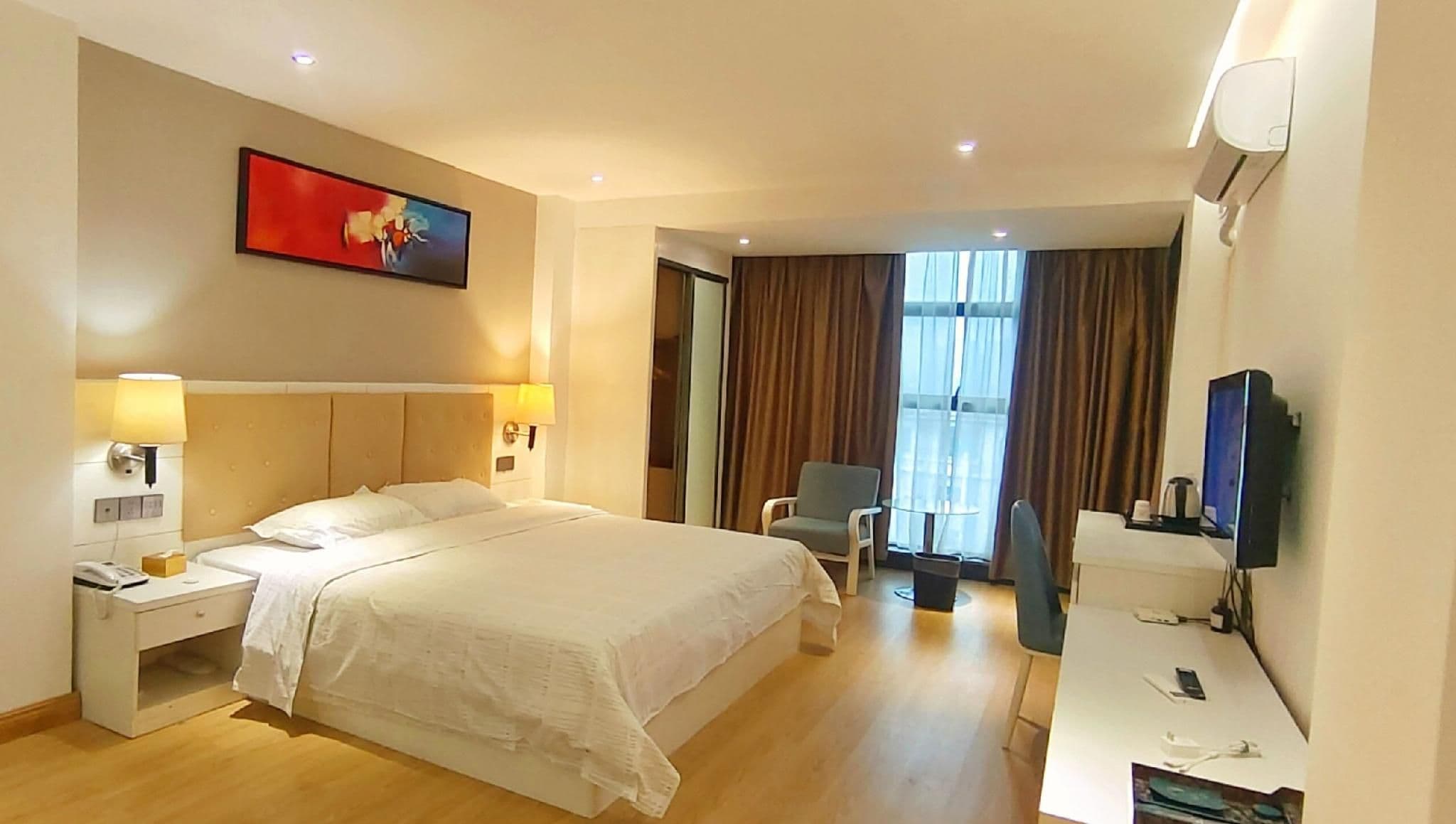 A hotel room with a large bed, bedside tables, a desk, a chair, a television, and a window with curtains.