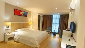 Habitación de hotel con una cama grande, mesitas de noche, un escritorio, una silla, un televisor y una ventana con cortinas.