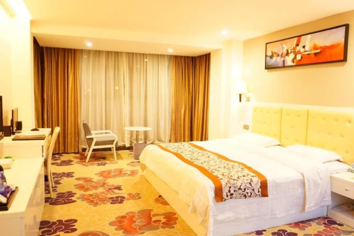 A hotel room with a bed, desk, chair, and curtains.