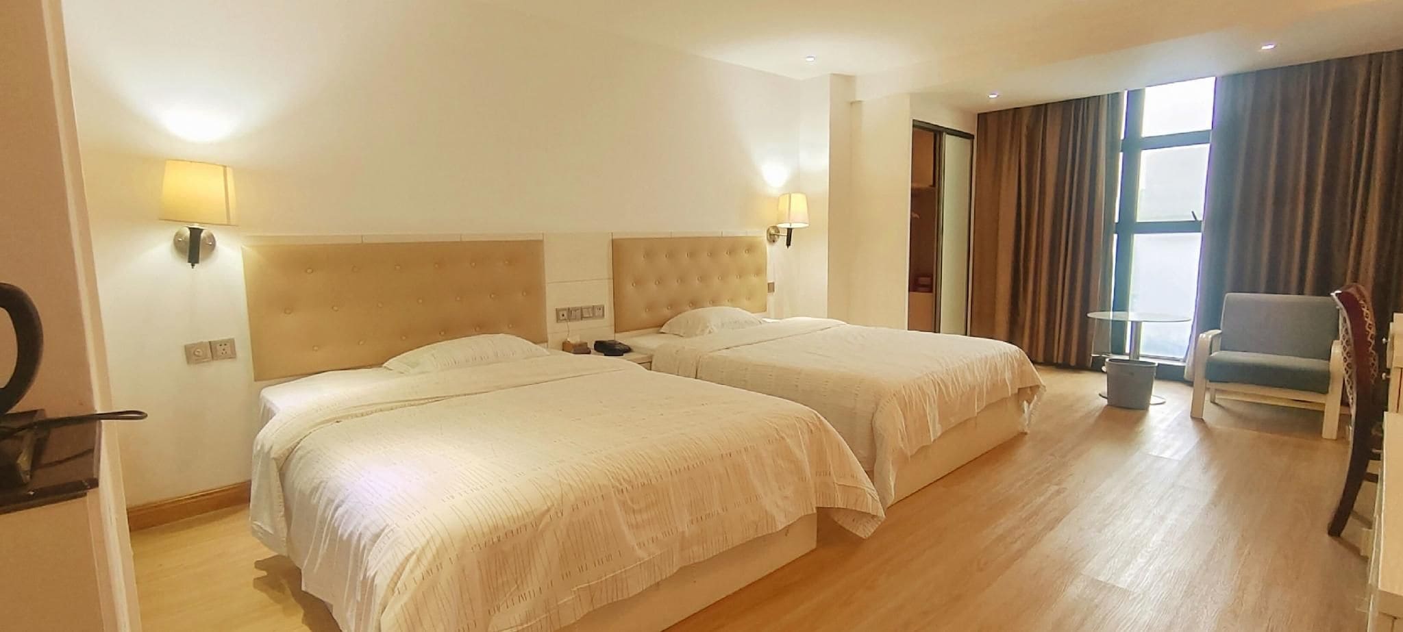 A hotel room with two beds, a chair, a desk, and a window with curtains.