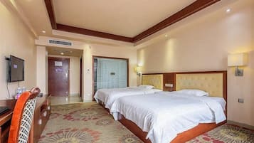 A hotel room with a large bed, a desk, a television, and a door leading to another room.