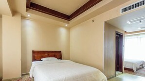 Une chambre d’hôtel avec un lit simple, une tête de lit en bois, une moquette à motifs et une porte donnant sur une autre pièce.