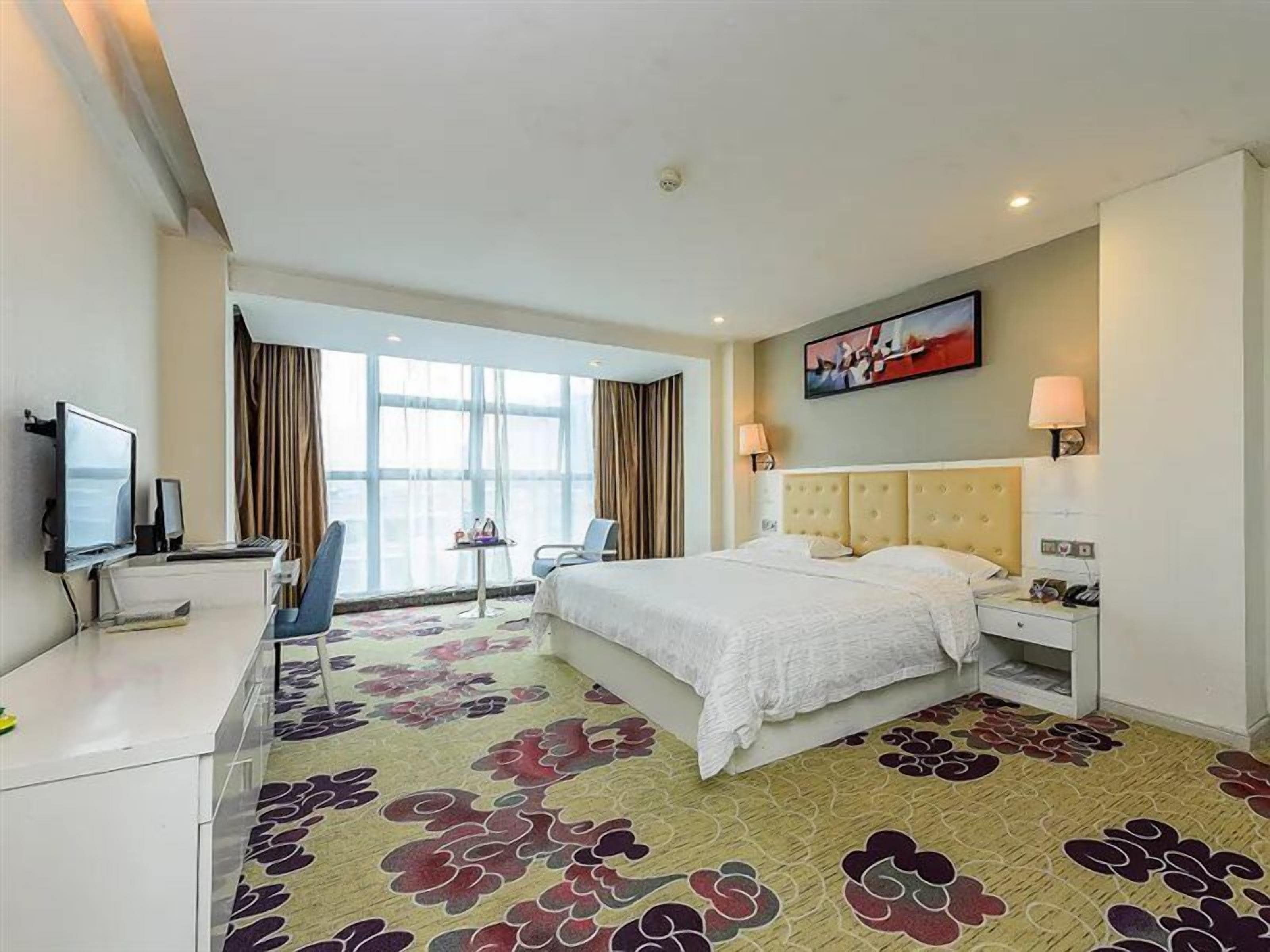 A hotel room with a bed, desk, chair, television, and a large window.