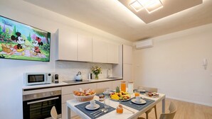 A modern kitchen with a dining table set for breakfast, a microwave, oven, and a TV displaying a cartoon. - Desenzanoloft Apa Dom  (Desenzano del Garda)