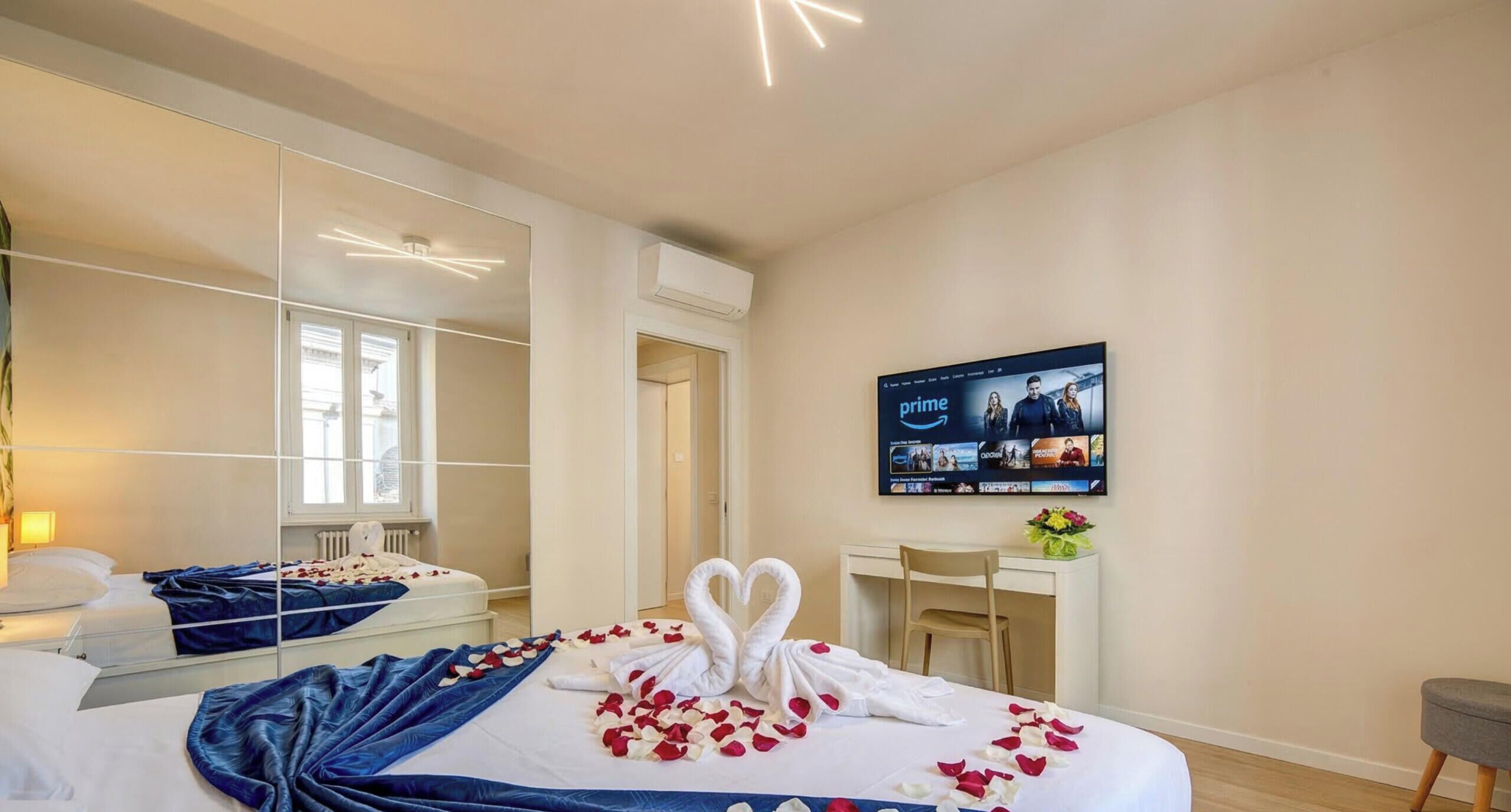 Una habitación de hotel con cama, escritorio, silla, televisor y espejo.