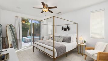 A modern bedroom with a four-poster bed, a ceiling fan, a bedside table with a lamp, and a view of a swimming pool through glass doors.
