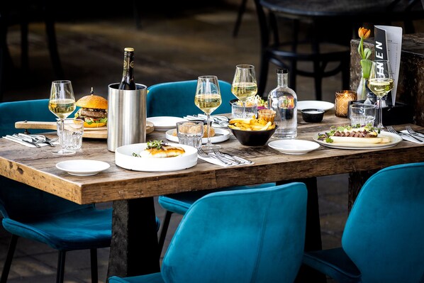 A wooden dining table set with plates, glasses, a bottle, and a menu. - Broeck Oudewater (Oudewater)