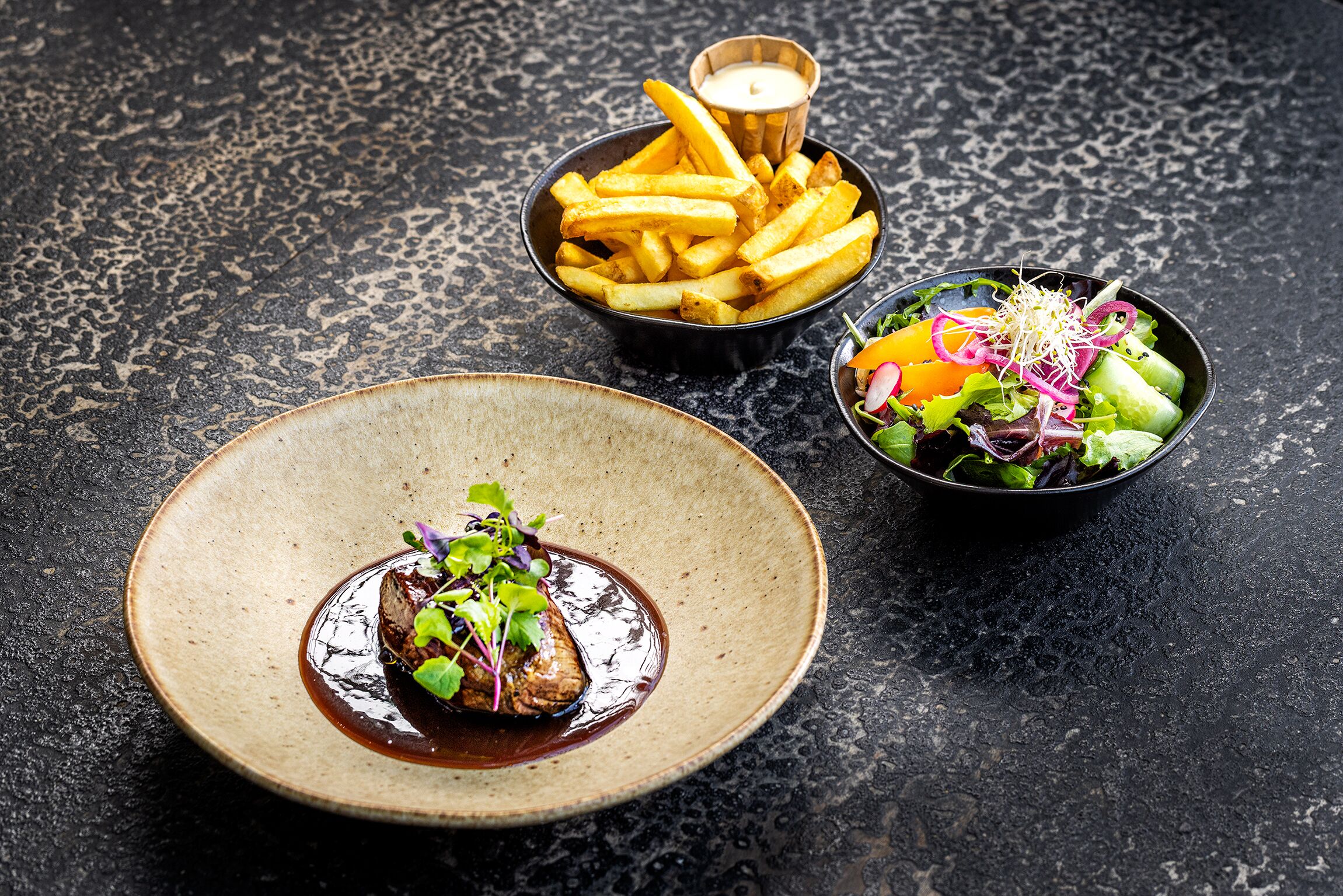 Une assiette de nourriture comprenant des frites et une salade, le tout posé sur une surface texturée.