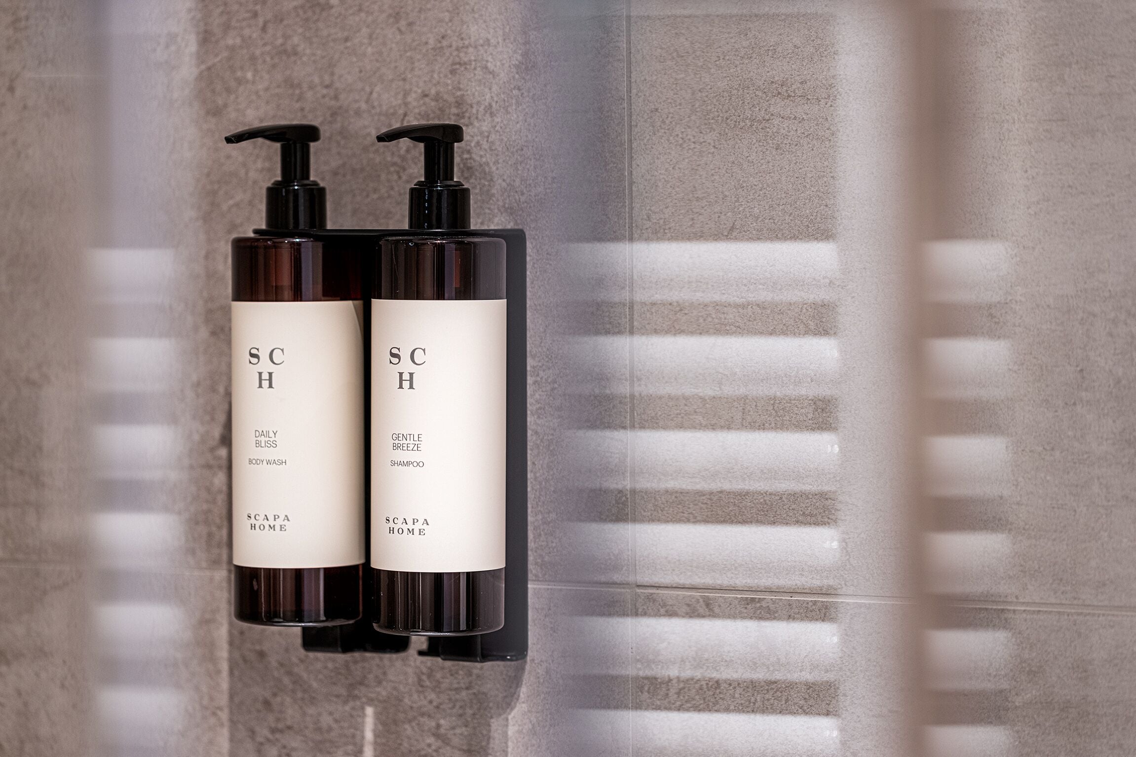 Two SCAPA HOME body wash bottles mounted on a textured wall.