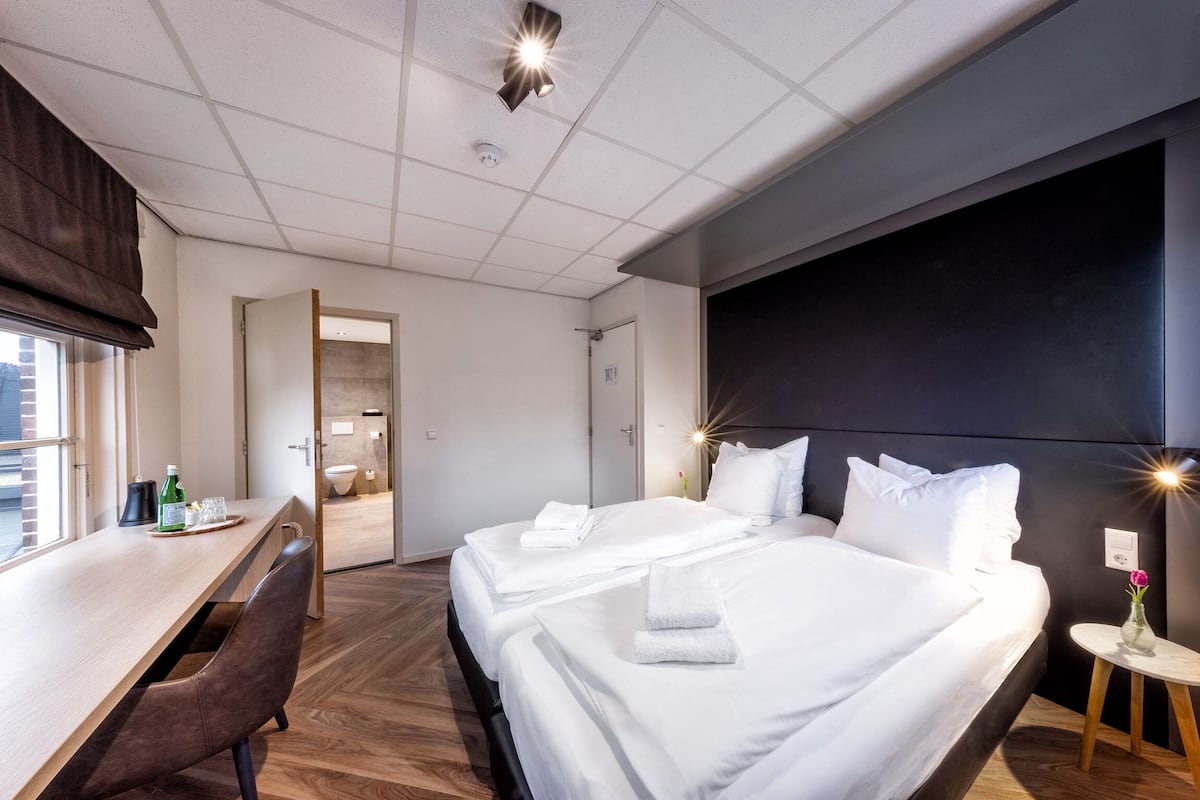 A modern hotel room with a large bed, a desk, and a shower area.