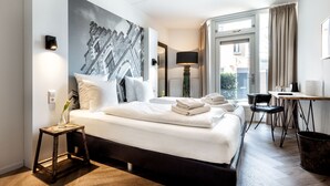 A modern hotel room with a large bed, a small side table, a desk with a chair, and a view of the city through the window. - Broeck Oudewater (Oudewater)