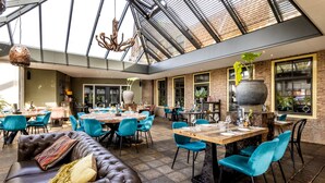 A spacious indoor dining area with high ceilings, exposed brick walls, and a variety of seating options including a leather couch and multiple tables with chairs. - Broeck Oudewater (Oudewater)