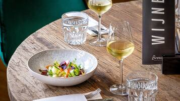 Et træbord med en salatskål, to glas hvidvin og en menu med teksten 'WIJNEN BROEO'.