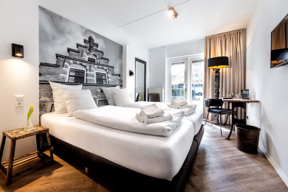 A hotel room with a large bed, a small table, a chair, a lamp, and a painting on the wall.