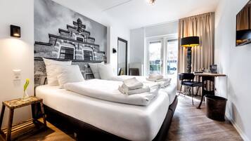 A hotel room with a large bed, a small table, a chair, a lamp, and a painting on the wall.