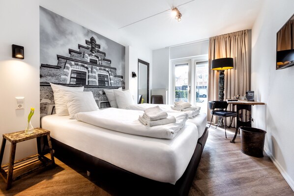 A hotel room with a large bed, a small table, a chair, a lamp, and a painting on the wall. - Broeck Oudewater (Oudewater)
