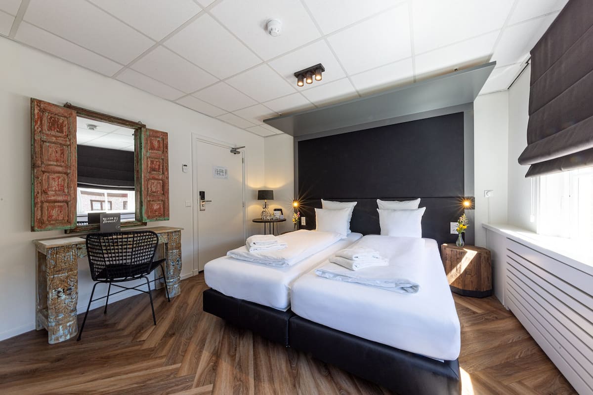 A hotel room with a large bed, a desk, a chair, and a mirror.