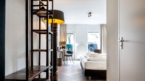 A hotel room with a wooden floor, a bed with white linens, a desk with a chair, and a hanging lamp. - Broeck Oudewater (Oudewater)