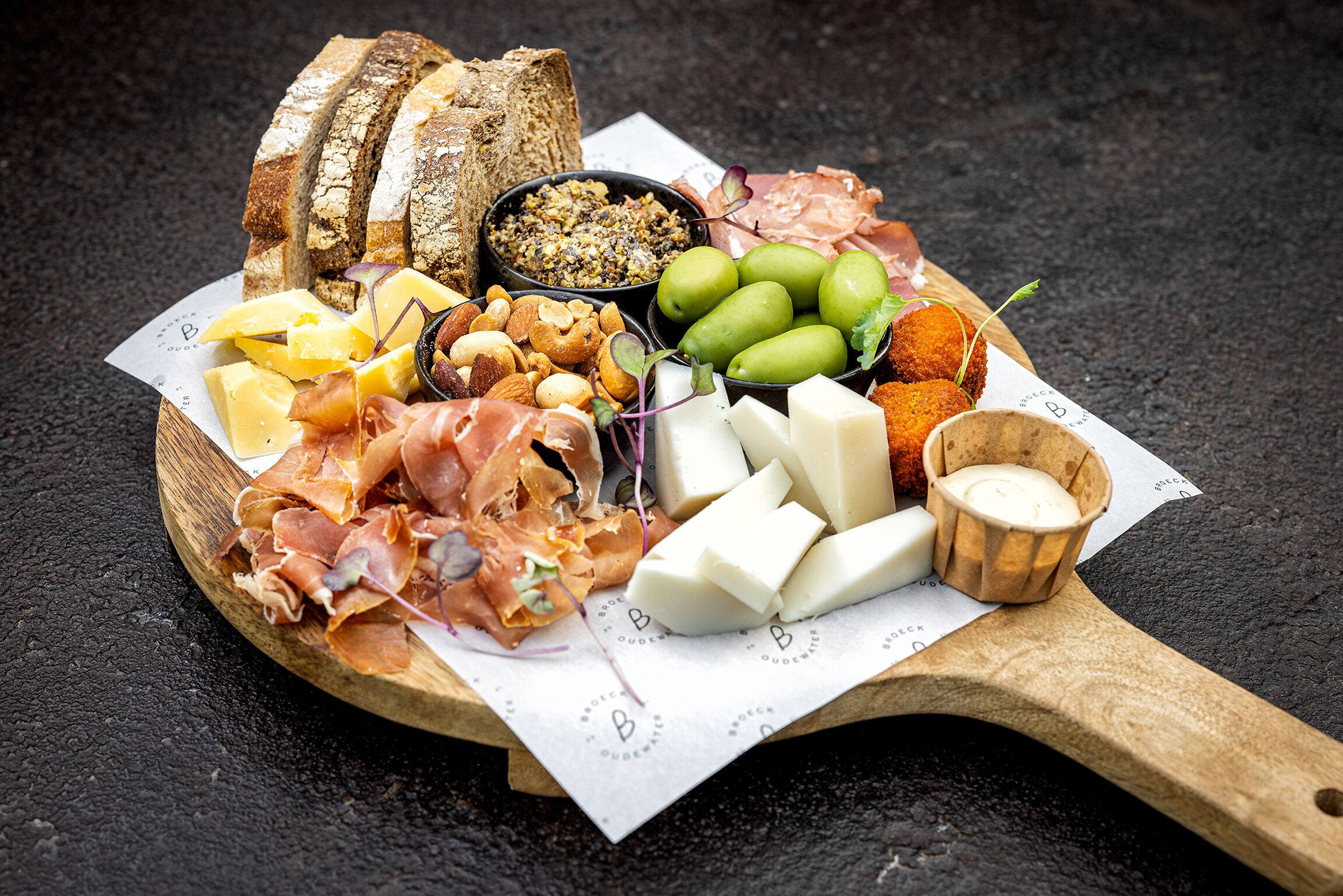 A wooden board with various cheeses, cured meats, and bread.