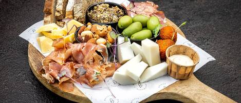 A wooden board with various cheeses, cured meats, and bread.