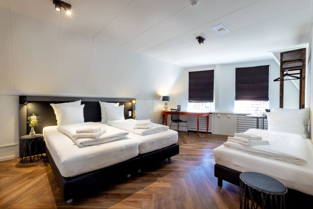 A modern hotel room with two beds, a desk, and a chair.