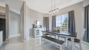 Un'elegante zona pranzo moderna con pavimento in marmo, tavolo in legno scuro, sedie bianche, un lampadario e un'ampia finestra con tende.