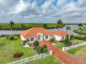 A large, single-story house with a red-tiled roof, surrounded by lush greenery and a body of water. - Spacious waterfront home with jaw-dropping views! (Port Charlotte)