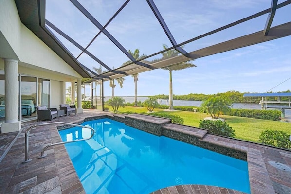 An indoor swimming pool with a clear view of the surrounding landscape, including palm trees and a body of water. - Spacious waterfront home with jaw-dropping views! (Port Charlotte)
