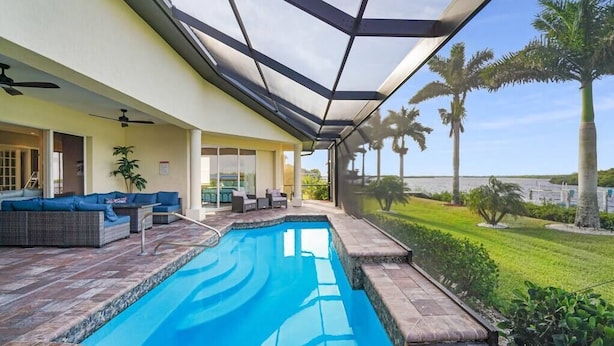 Una piscina con un patio vetrato, mobili da esterno e palme sullo sfondo.
