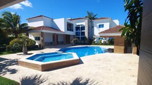 A modern house with a swimming pool, surrounded by palm trees and a clear blue sky.