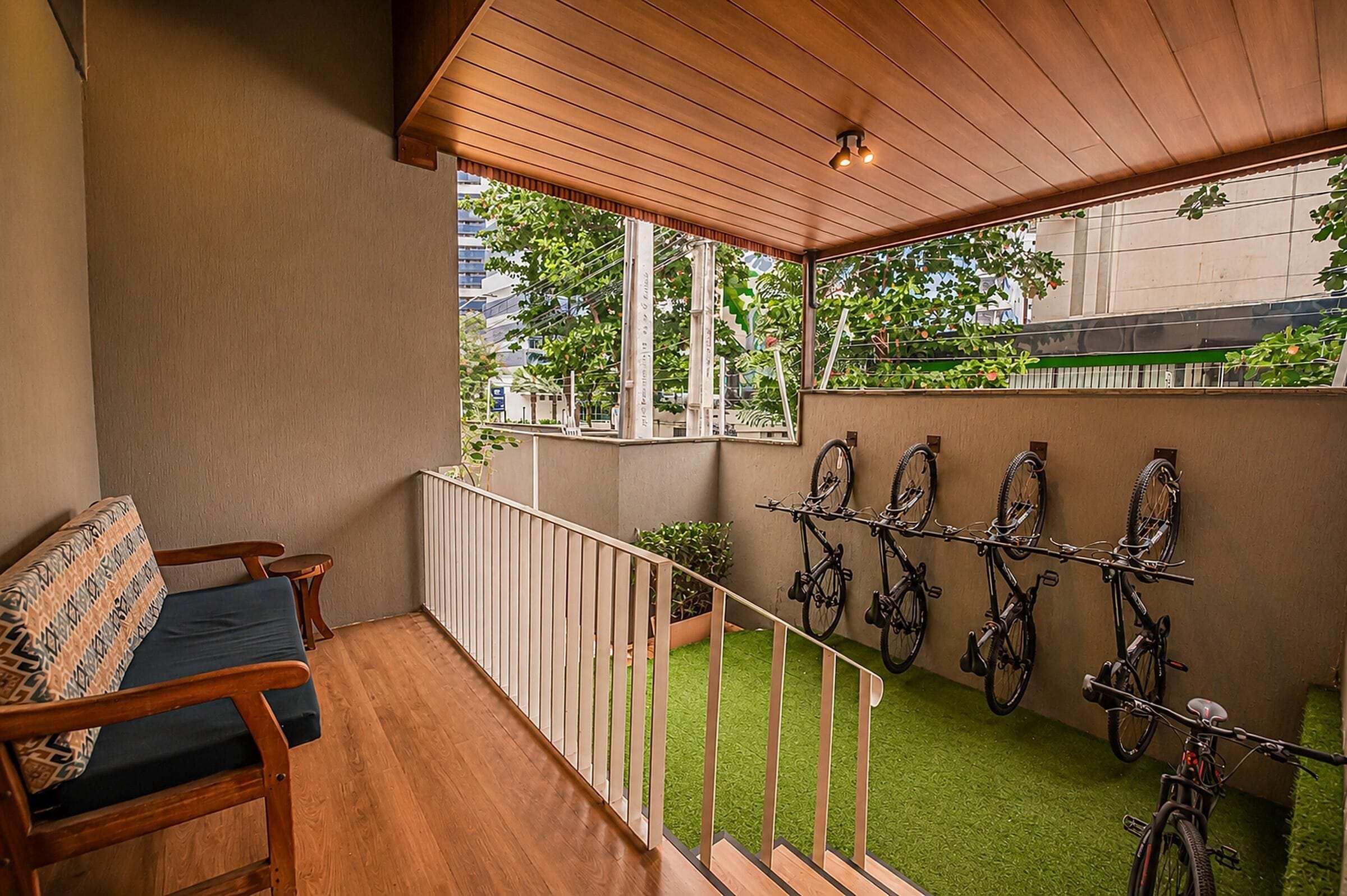 A balcony with a wooden floor, a sofa, a railing, and bicycles mounted on the wall.