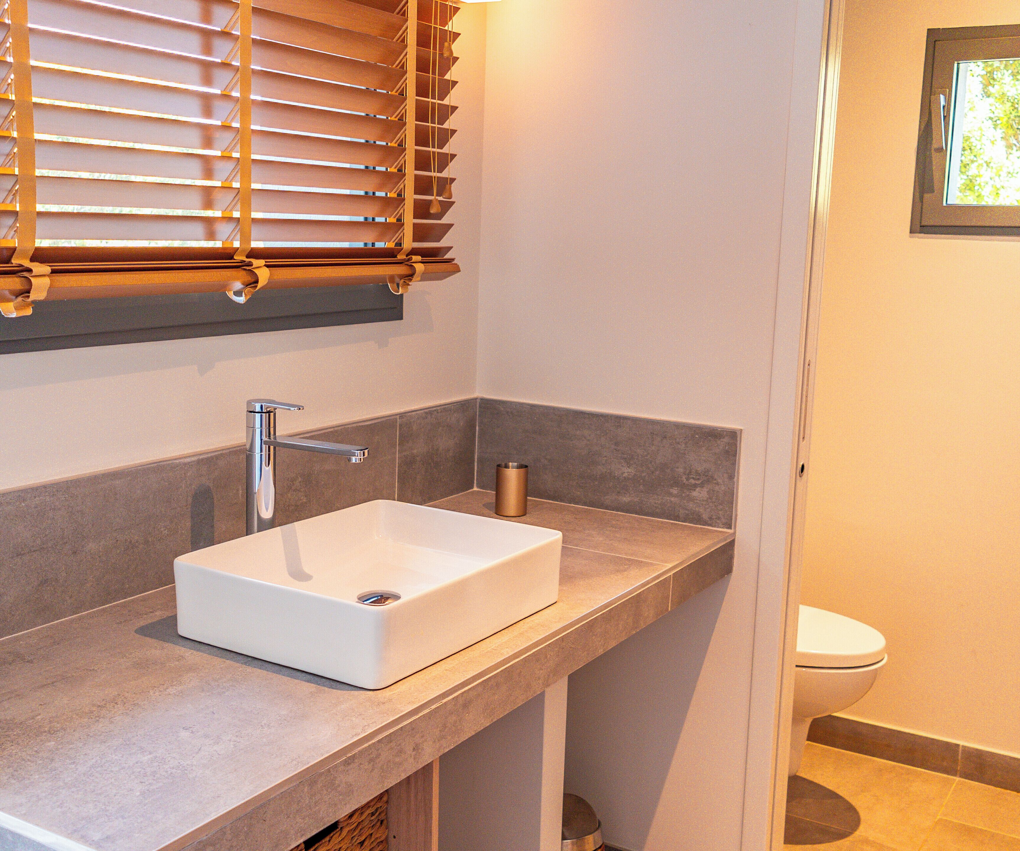 A modern bathroom with a white sink, a shower, and a toilet.