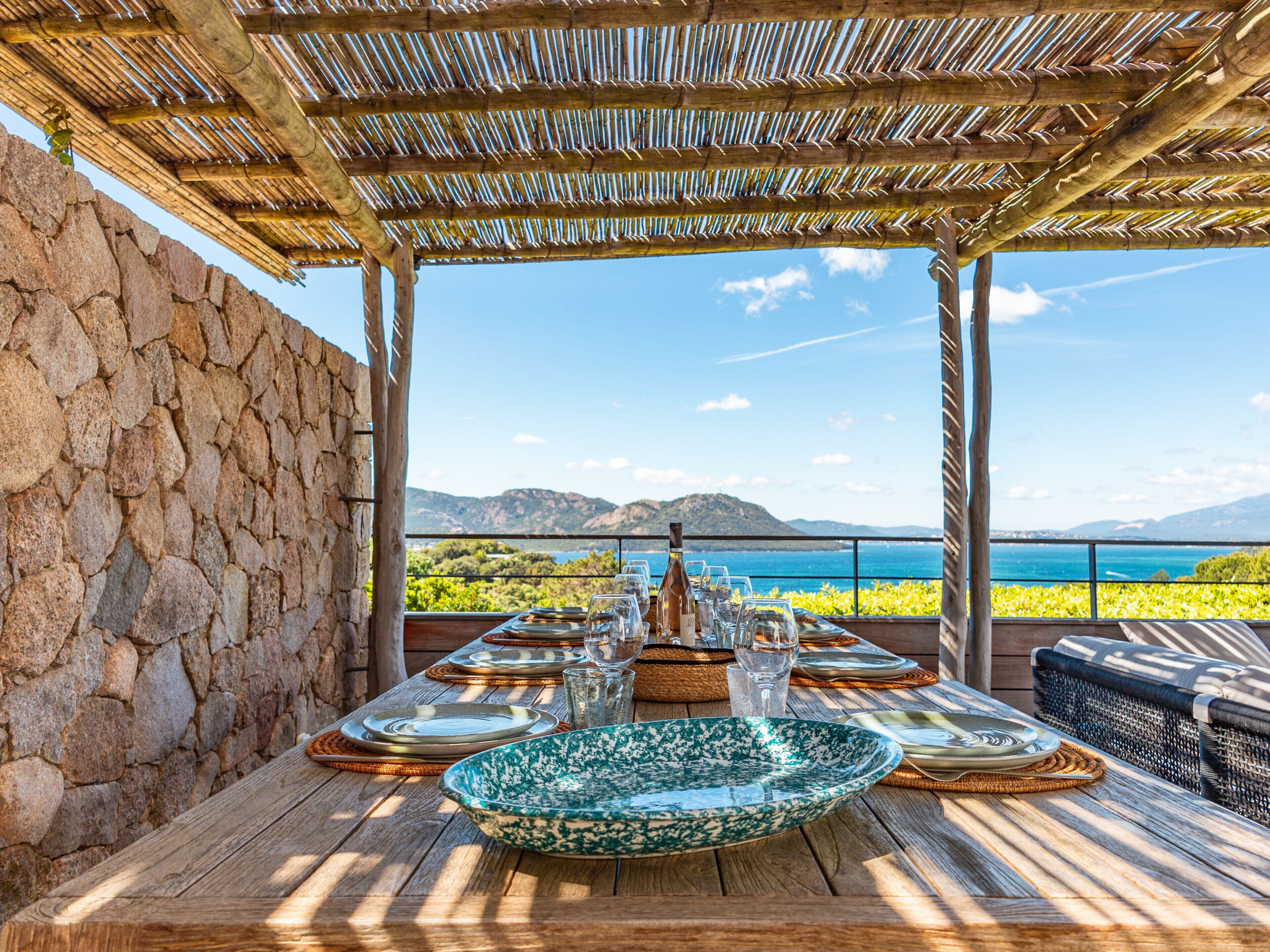 A wooden table set for dining with a view of the sea and mountains.
