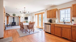 Une cuisine spacieuse avec des meubles en bois, un coin repas comprenant une table et des chaises, une cheminée et une grande fenêtre.