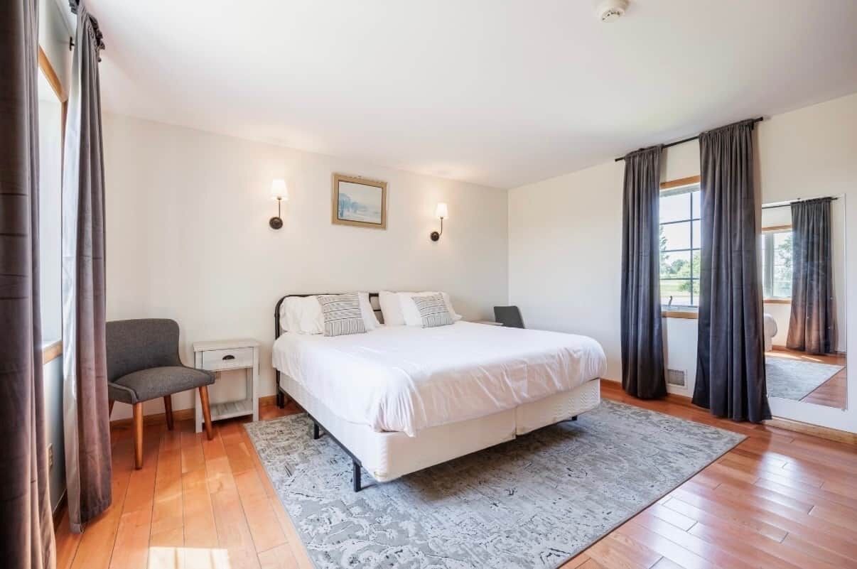 Un dormitorio con una cama, mesitas de noche, una silla, una alfombra y un cuadro en la pared.