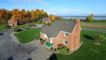 A large brick house with a green porch, surrounded by a well-maintained lawn and trees with autumn foliage.