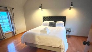 Een slaapkamer met een groot bed, houten vloeren, twee wandlampen en een raam met gordijnen.
