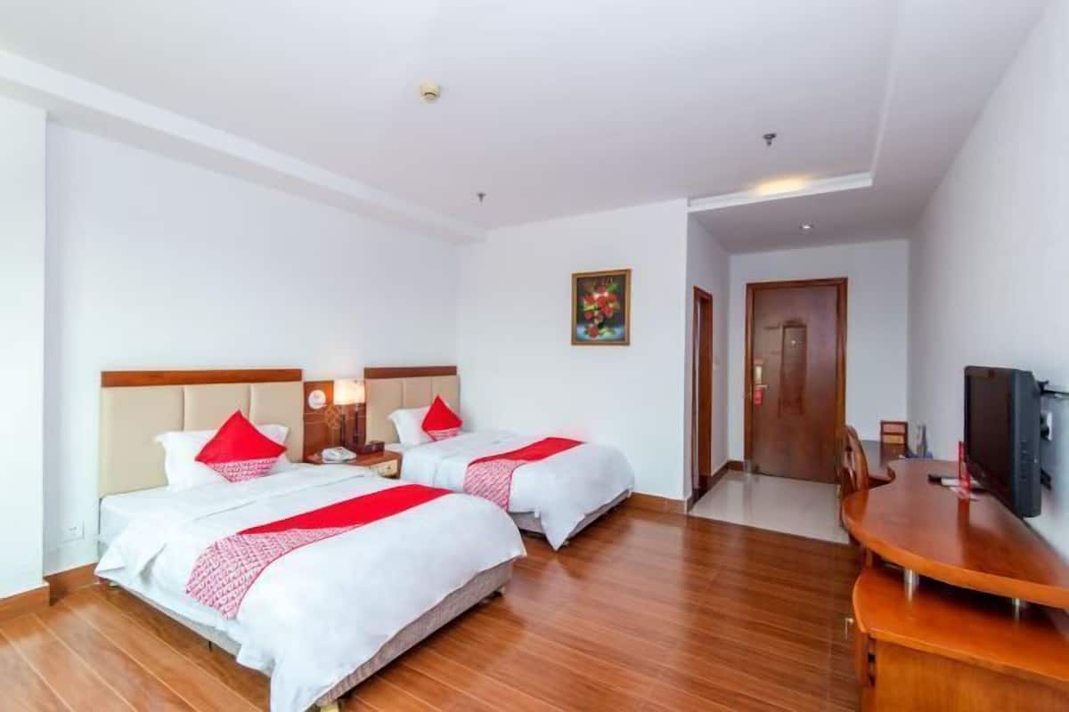 A hotel room with two beds, a wooden desk, a television, and a door leading to another room.