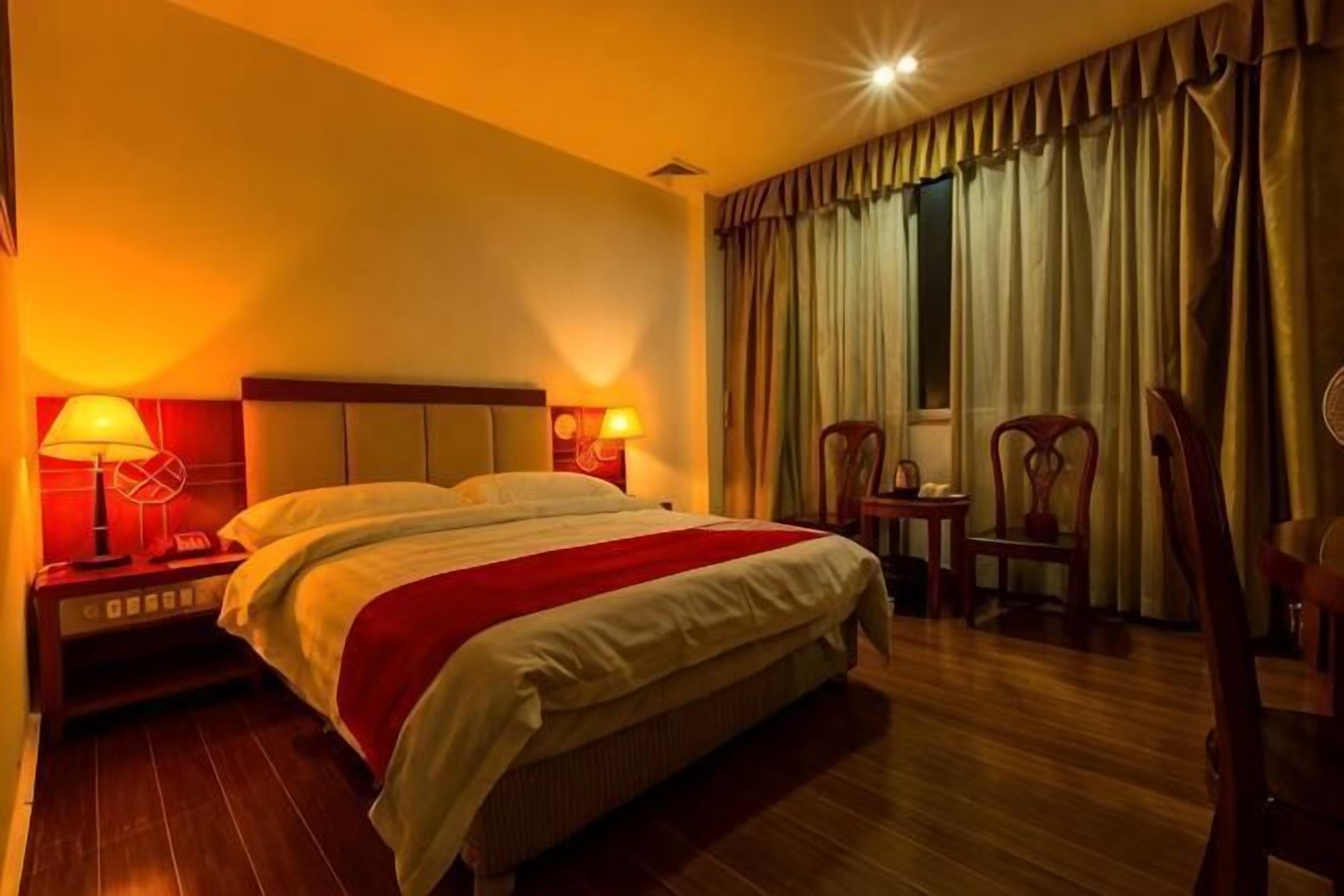 A hotel room with a bed, nightstands, lamps, and curtains.