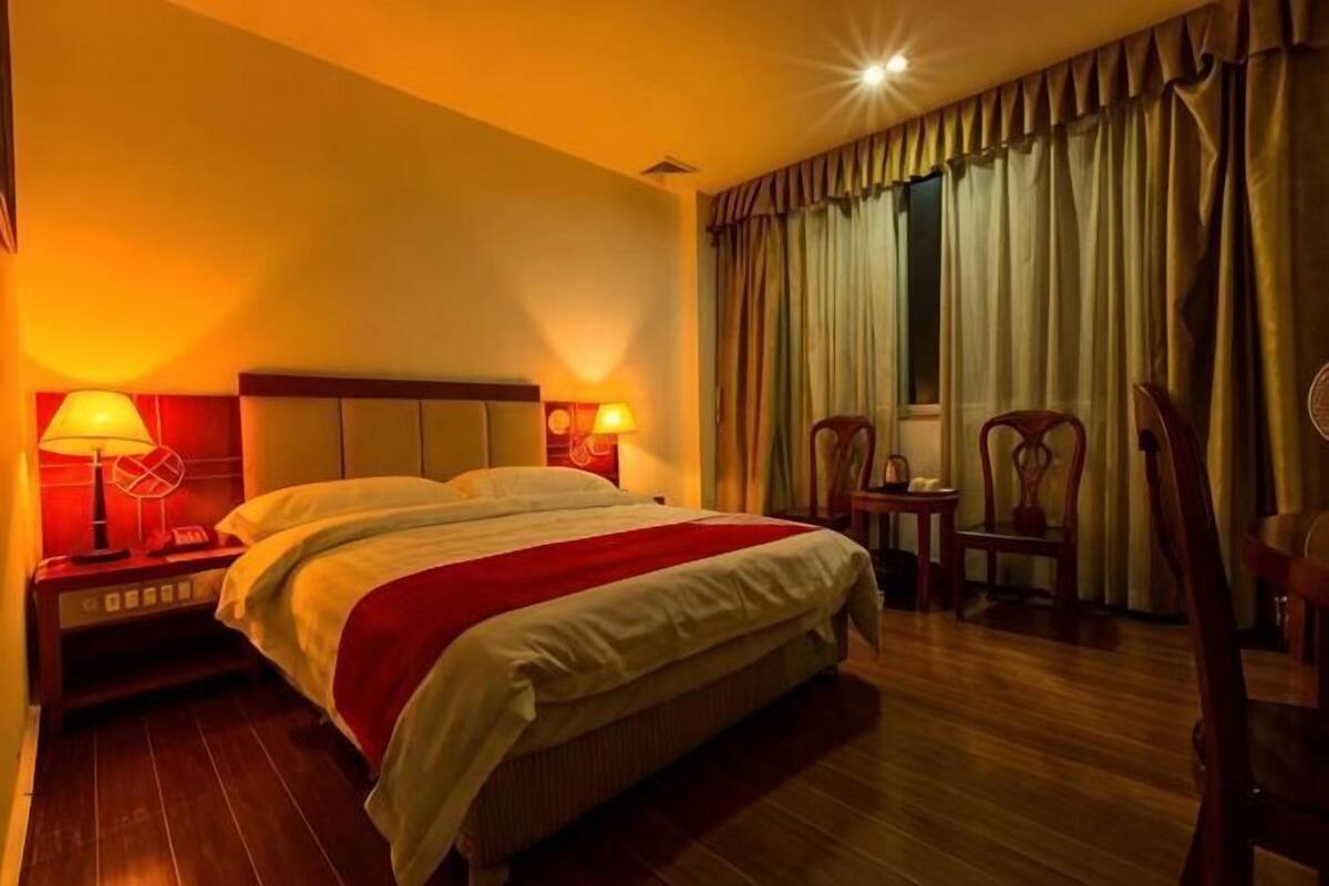 A hotel room with a bed, nightstands, lamps, and curtains.
