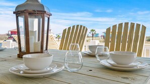 Una mesa dispuesta con cuencos y vasos blancos, un farol y sillas de madera, con vistas a palmeras y edificios al fondo.