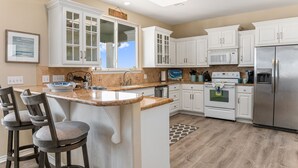 Una cocina moderna con armarios blancos, una isla central con taburetes, un refrigerador de acero inoxidable y un microondas.