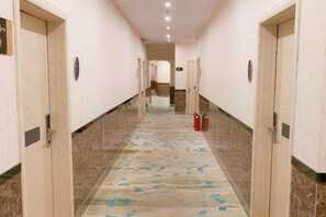 Un couloir d’hôtel avec des portes des deux côtés, une moquette à motifs et un extincteur posé sur le sol.