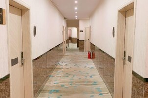 Pasillo de hotel con puertas a ambos lados, una alfombra estampada y un extintor en el suelo.