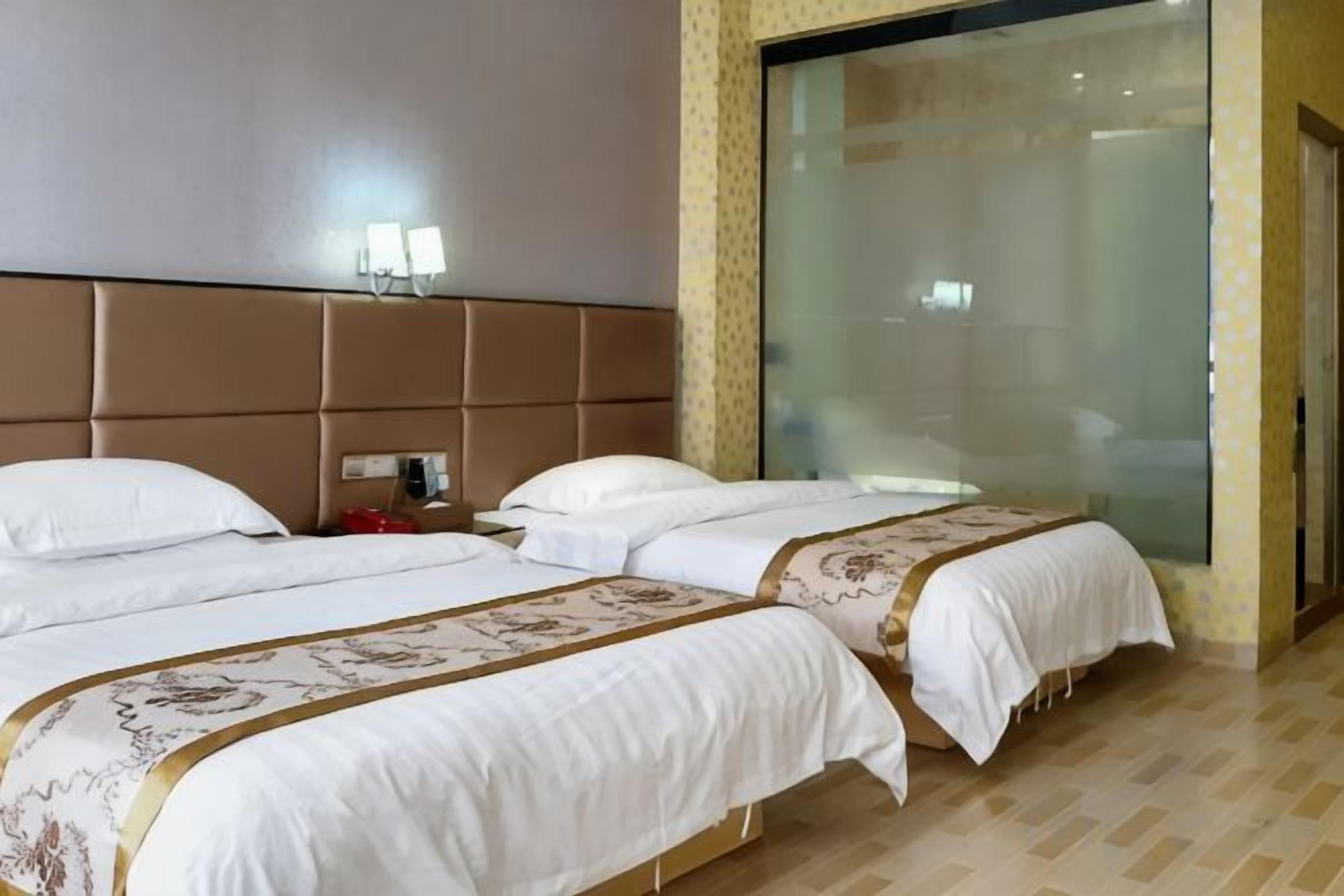 A hotel room with two beds, a large window, and a wall-mounted light fixture.