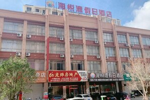 A multi-story hotel with a red and beige facade, multiple air conditioning units, and several storefronts at the ground level. - Haiyuewan Holiday Hotel (Fangchenggang)