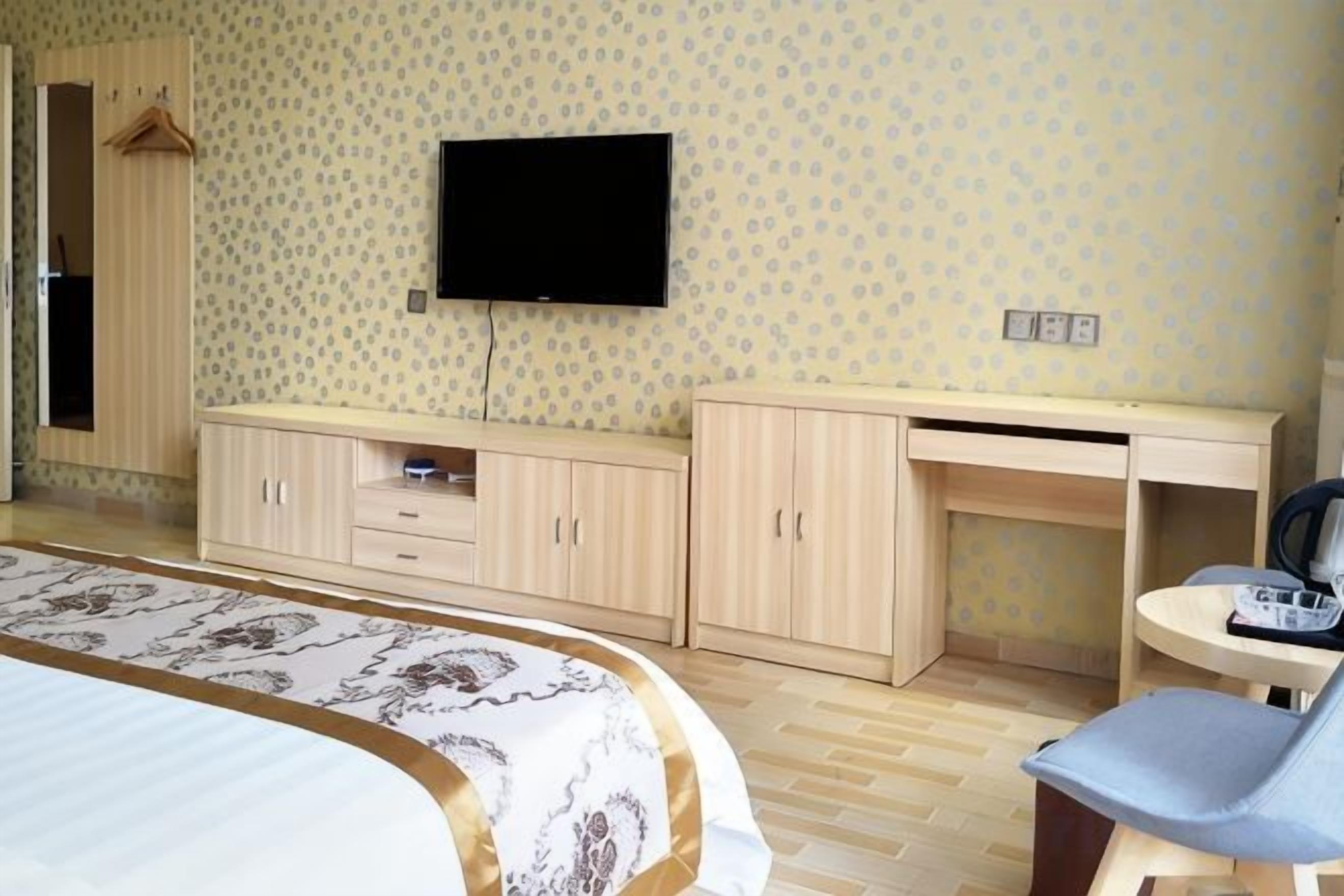 Quarto de hotel com cama, escrivaninha, cadeira, televisão e guarda-roupa.